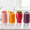 Six different smoothies in glasses arranged on a countertop
