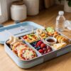 Easy school lunch ideas in a colorful bento box with mini pizzas, sandwiches, roll-ups, fruit, vegetables, pancakes, and quesadilla triangles.
